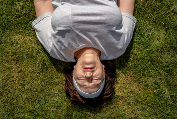 Senior woman lying on the grass. She lying and down her hands. Portrait. She is happy and smiles. Eyes is closed. Old ages healthy lifestyle concept. Summer. Top view