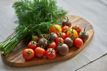 Composition of tomatoes and dill on a wooden table.Different color tomatoes and fresh green dill on a cutting board.