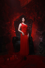 beautiful lonely girl in long red dress on the halloween throne ready for scary party