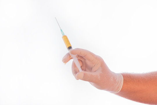 Photo detail of a syringe full of medicine held by the hand of a doctor covered by a medical glove on a white background. Space for writing.