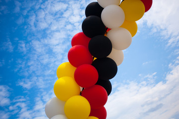 Balloons - Colors of the German National Flag (black, red, yellow)  - outdoors against blue Sky with white Clouds - Symbol for Festivity or Celebration