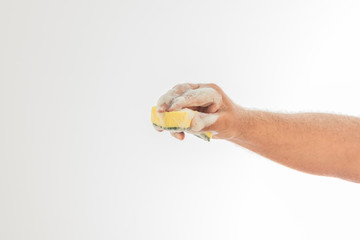 A man's hand full of white foam holding a dishwashing sponge on a white background.