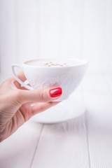 Female hand holding white porcelain cup of coffee cappuccino with cinnamon. Manicure with red nail polish. Copy space