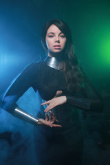 futuristic fashion model wearing black and silver clothes and standing in the colorful blue and green smoke