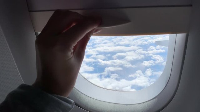 woman hand is opening  window of airplane. Clouds and sky as seen through window of an aircraft, air plane.