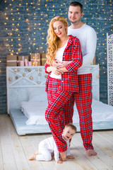 Loving happy couple husband and wife in plaid pajamas stand near the christmas lights of garlands. Festive mood. Merry christmas and happy new year.