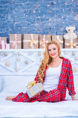 Beautiful young blond woman in checkered pajamas with New Year's gifts. Merry christmas and happy new year.