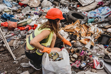 Woman volunteer helps clean the field of plastic garbage. Bushes and sky in the background. Earth day and ecology.