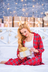 Beautiful young blond woman in checkered pajamas with New Year's gifts. Merry christmas and happy new year.