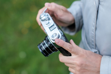 Female hands holding retro photo camera and push winding lever on background grass.
