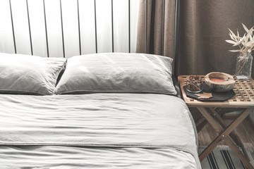 Cozy gray bedroom interior with comfortable bed near the wooden night table with candle, cinnamon and dry leaf. Cozy atmosphere at home. Warming up the cold winter or autumn evenings.