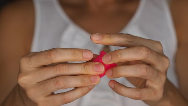 Woman holding a new pink menstrual cup in hands and showing how to make C-fold to insert it