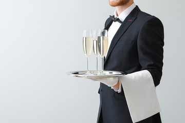 Handsome waiter with champagne on light background