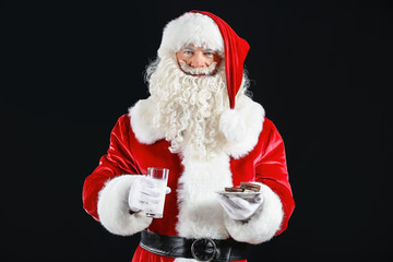 Santa Claus with milk and cookies on dark background