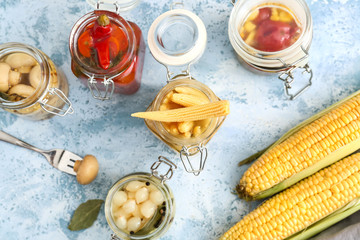 Jars with different canned vegetables on color background