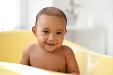 Little African-American baby washing in bathtub at home