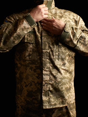 Ukrainian soldier dressed in uniform stands in the dark and fastens his jacket