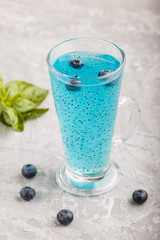 Glass of blueberry blue colored drink with basil seeds on a gray concrete background.  Side view