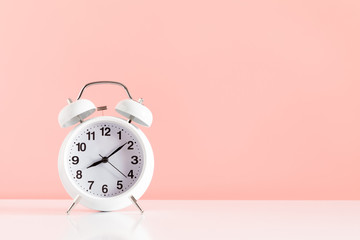 White alarm clock on pastel pink background. Trendy minimalist style. copy space