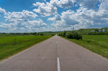 Two-lane countryside road among green fields and meadows