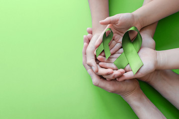 Adult and child hands holding Lime Green Ribbon on green background, Mental health awareness and...