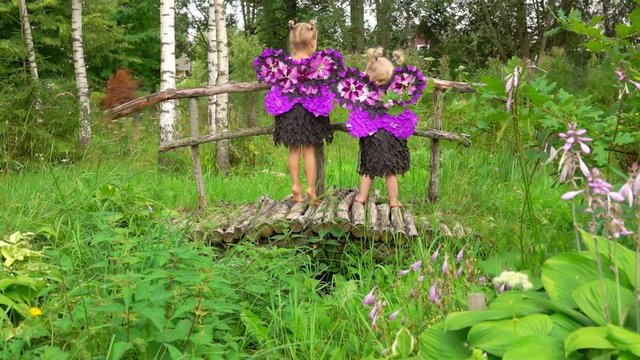 Happy girls in purple butterfly costumes play on the wooden bridge. Fairytale story