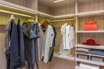 modern wooden wardrobe with clothes hanging on rail in walk in closet