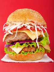Meat burger with  vegetables on a red background.Double cheeseburger with fresh tomatoes, lettuce, onions, and chopped cabbage.