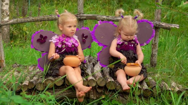 Girls with butterfly wings eat honey from pots. Children pretend to be purple butterflies