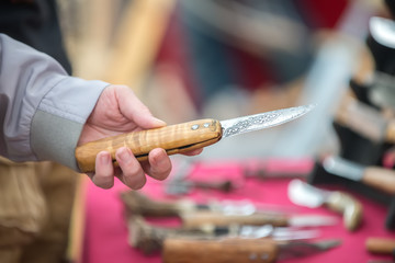A handmade knife with a metal blade and a wooden handle in a man's hand at the fair. The concept of craft and needlework.