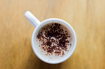 Coffee with foam and chocolate mug in a white mug on a wooden table. Cappuccino in a white mug on a light background. Good morning. Morning cappuccino for breakfast. Coffee in a mug top view. 