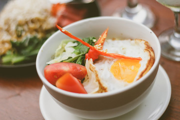 Spicy fried noodles in a bowl with fried egg, vegetables  and chili in a bowl as a complement and decoration on it