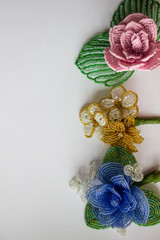 Three beaded flowers on a white background. Right side of the background with flowers. Blue, pink, gold flowers.