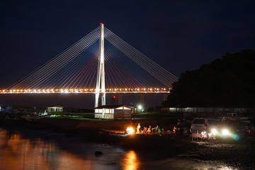 Night landscape with views of the Russian bridge. People relax on the beach.