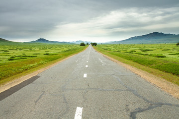 The road between the picturesque green meadows against a backdrop of sky, Mongolia.
