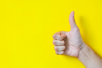 Close up of male hand showing thumbs up sign over yellow background with copy space, flat lay