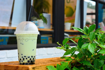 glass of milk bubble matcha green tea with tapioca pearls on wooden table with green leaves on blurred cafe restaurant background