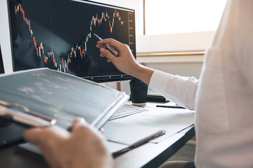 Investor man analyzing the graph of the stock market using a pen pointing to the computer screen.