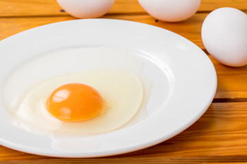 木の背景に白いお皿に生卵が乗っているコピースペース、朝食、料理用