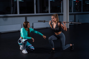 Young athletic girl lunges with a barbell in the gym under the supervision of a trainer. Female...