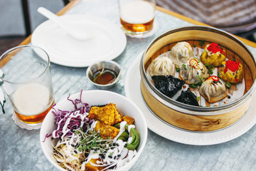 Pan-Asian food - different dim sums in bamboo bowl and salad. Lunch for two with beer
