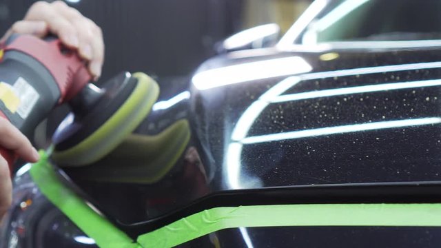 Worker finish polishing new expensive car, on hood are pieces of polishing disc