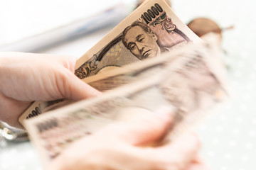 Close up hands of a woman counting ten thousands banknotes Japanese Yen. Cash based society, Currency exchange, Economics, Financial, Lending, Investment, Saving, Conversion rates, Commission, Money.
