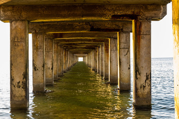 View under a long wooden pier with pillars standing in the water
