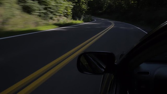 An exterior angle of a car driving through a shaded rural back-road as multiple cars pass on the opposite side.