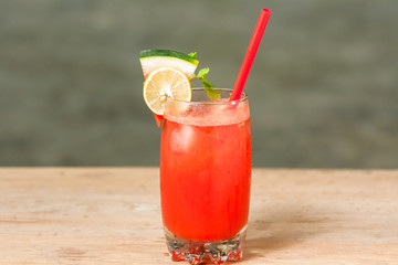Side view of a glass of  Water melon juice with red straw garnished with a  slice of lemon, watermelon and mint leafs 