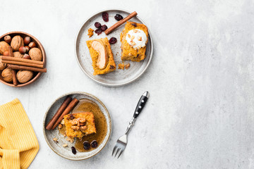 Apple and pumpkin cake slice with walnuts, maple syrup and cream on a plate, grey concrete background. Top view, copy space. Autumn comfort food