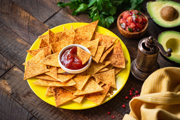 Mexican tortilla chips Nacho with tomato sauce and salsa on yellow plate, wooden background. Tex mex food