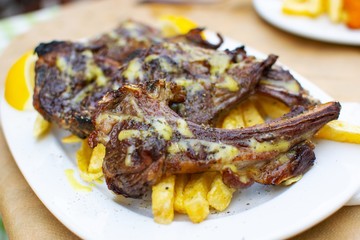 Lamb chops with french fries in a white plate close up.
