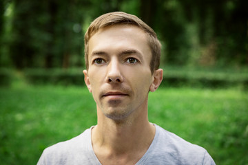 Portrait of the pacified face of a young attractive man  against the background of green foliage.